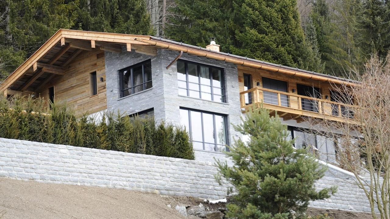 Ein geräumiges Haus aus Holz und Stein mit vielen Fenstern auf einer Anhöhe.