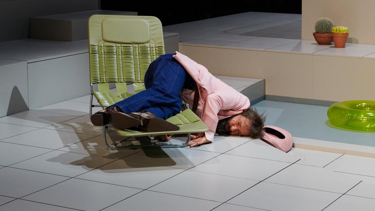Schauspieler Michael Neuenschwander liegt im Stück "Kurze Interviews mit fiesen Männern" am Schauspielhaus Zürich in einer ungelenken Körperhaltung halb auf dem Boden und halb auf einem Liegestuhl.