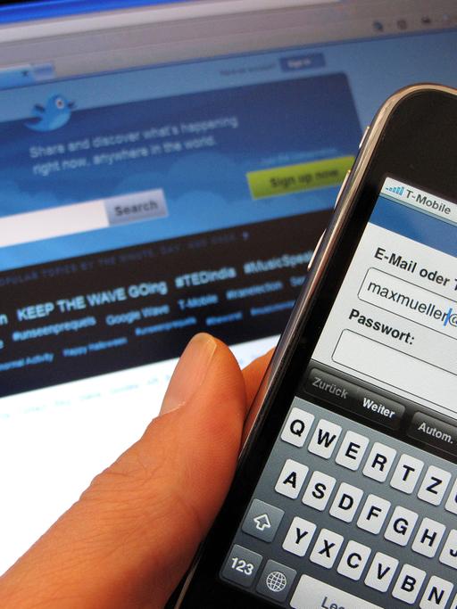 Facebook-Anmeldemaske auf einem Smartphone, während auf dem Bildschirm im Hintergrund die Startseite für den Kurznachrichtendienst Twitter zu sehen ist.