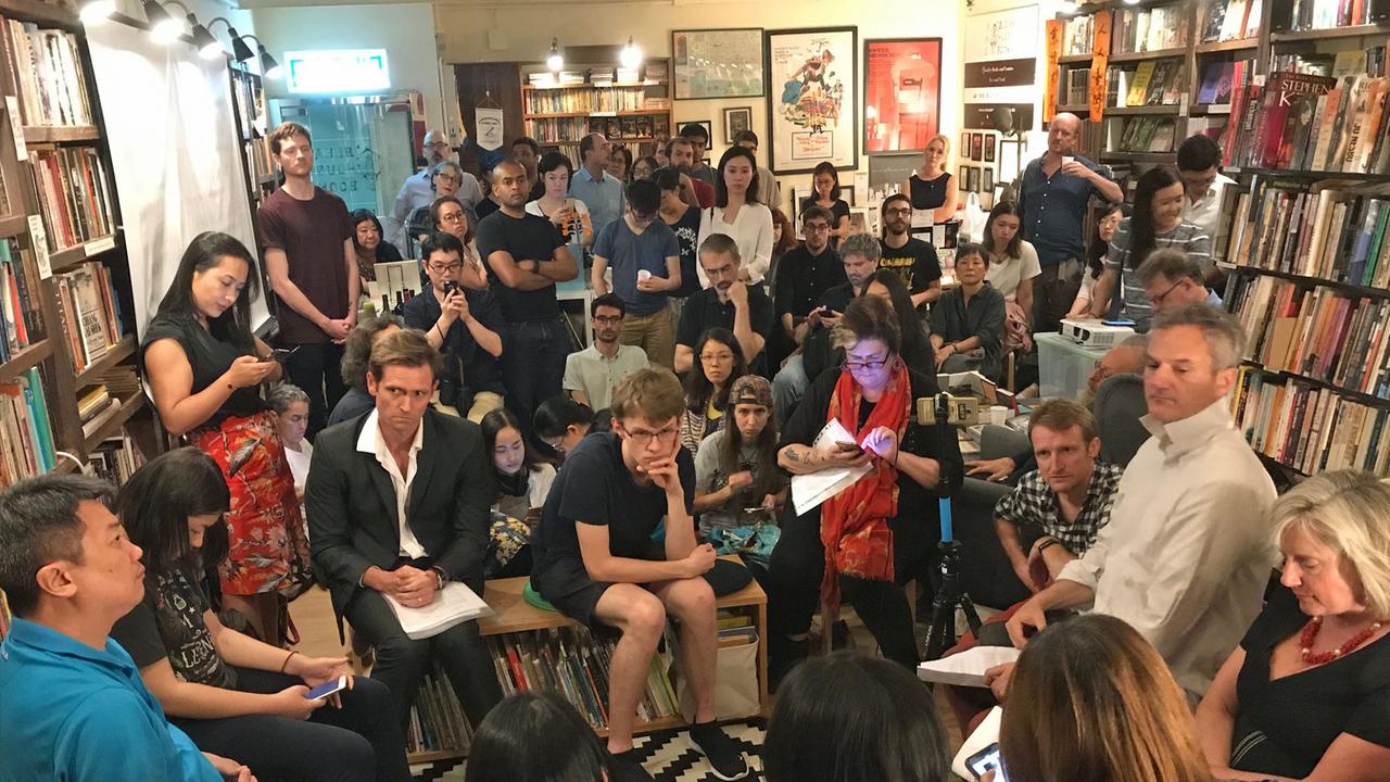 Blick auf die Zuhörer der Lesung von Tammy Ho in einer Buchhandlung. Die Zuschauer sitzen  dichtgedrängt auf Stühlen, Tischen oder auf dem BOden. Viele haben SMartphones in der Hand. Die Wände sind mit Bücherregalen vollgestellt.