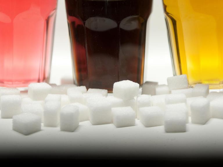 Drei Gläser gefüllt mit roter Limonade, Cola und Energy-Drink stehen am 23.08.2016 in Berlin neben Zuckerwürfeln auf einem Tisch.