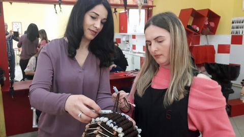 Zwei Frauen drehen Lockenwickler an einem Übungskopf mit Perücke ein
