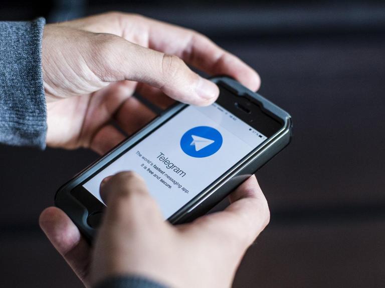 Zwei Hände halten ein Telefon auf dem der Messenger Telegram installiert ist.
