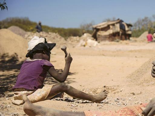 Ein Kind und eine Frau arbeiten in Lubumbashi in der Demokratischen Republik Kongo an Steinen aus einer Kobalt-Mine. Sie sitzen im Staub.