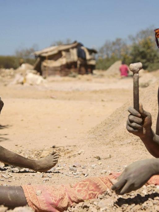 Ein Kind und eine Frau arbeiten in Lubumbashi in der Demokratischen Republik Kongo an Steinen aus einer Kobalt-Mine. Sie sitzen im Staub.