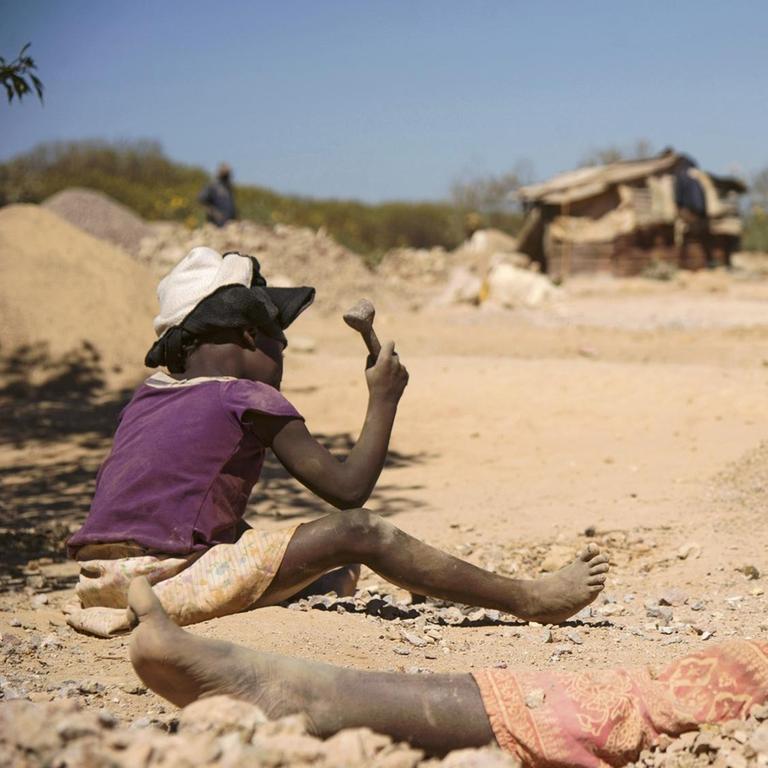 Ein Kind und eine Frau arbeiten in Lubumbashi in der Demokratischen Republik Kongo an Steinen aus einer Kobalt-Mine. Sie sitzen im Staub.