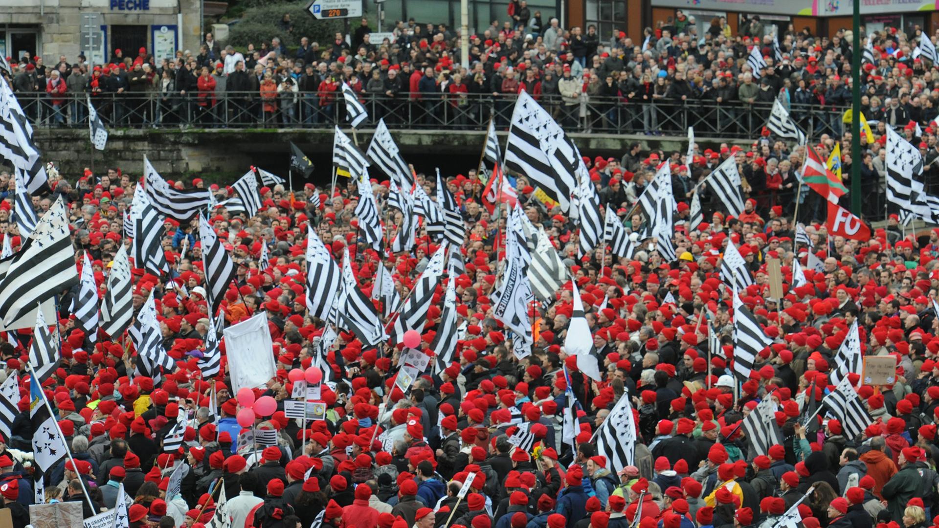 Blick von oben auf eine protestierende Menschenmenge mit roten Mützen und Fahnen in Quimper in der Bretagne