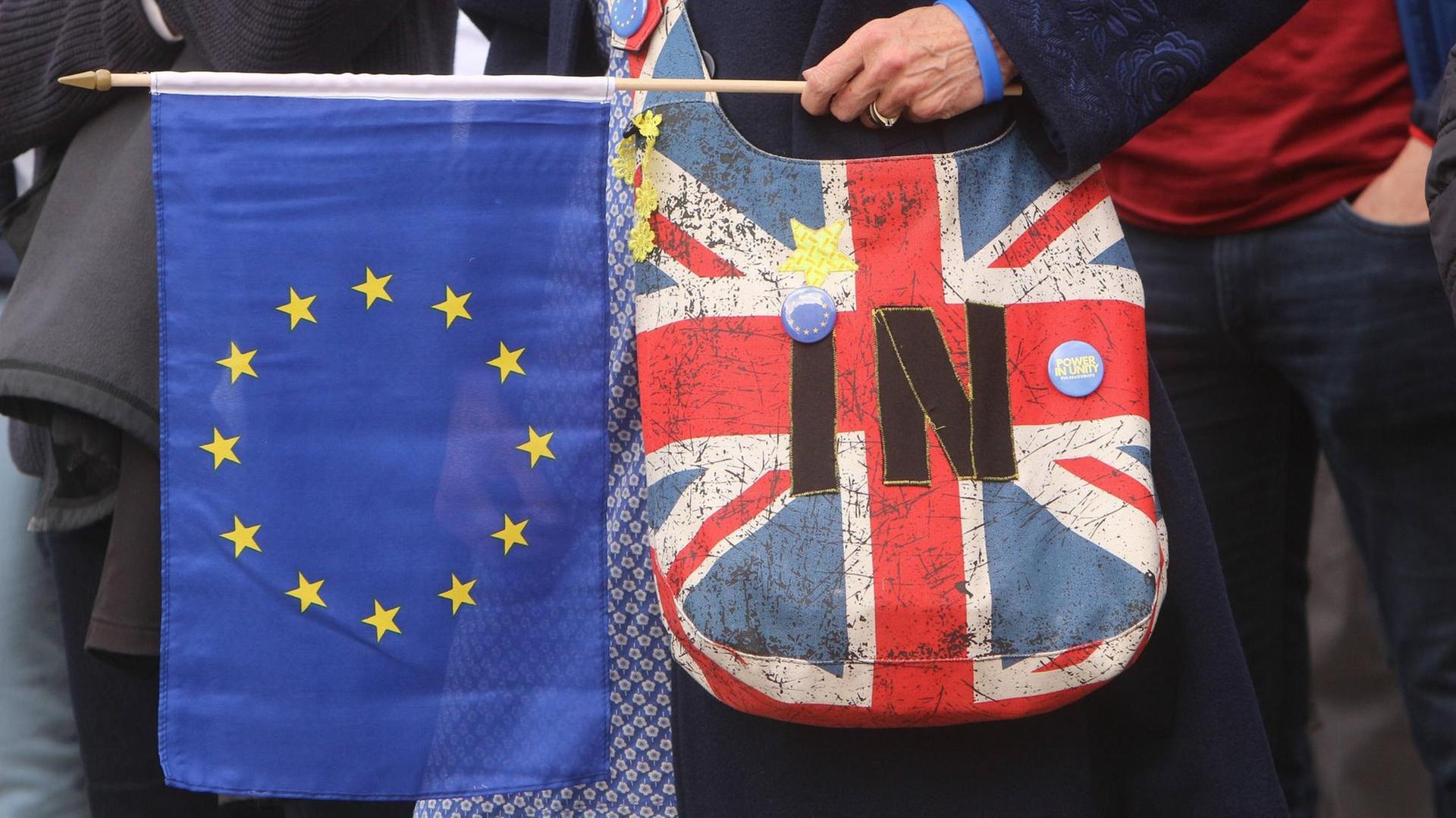 Frau mit einer Umhängetasche in den Farben der britischen Nationalflagge hält ein EU-Fähnchen