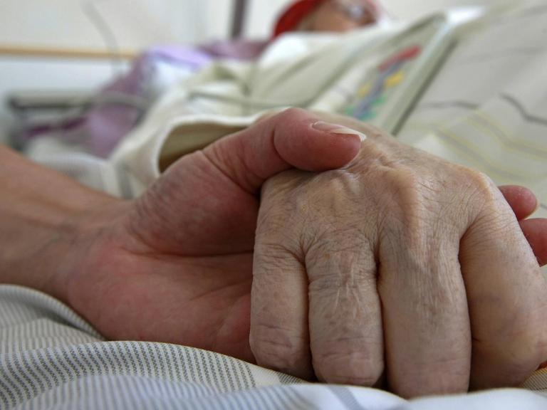 Großaufnahme einer Hand, die auf einem Krankenbett die Hand eines Intensivpatienten hält.