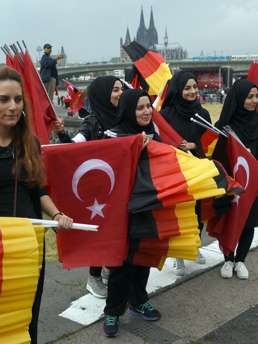 Türkische Frauen verteilen vor Beginn einer Kundgebung von Erdogan-Anhängern in Köln deutsche und türkische Fahnen.
