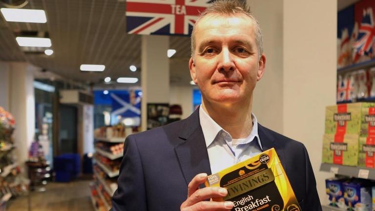 English-Shop Geschäftsinhaber Alexander McWhinney steht in einem Gang seines Ladens und hält eine Packung Tee in der Hand. Im English-Shop gibt es spezielle britische Produkte, die in Deutschland nicht breit vertrieben werden.