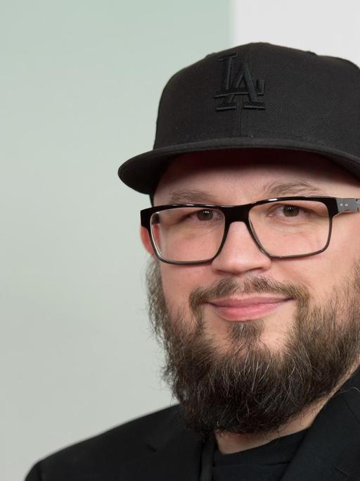 Christian Alvert trägt ein schwarzes Shirt, ein schwarzes Sakko und eine schwarze Mütze