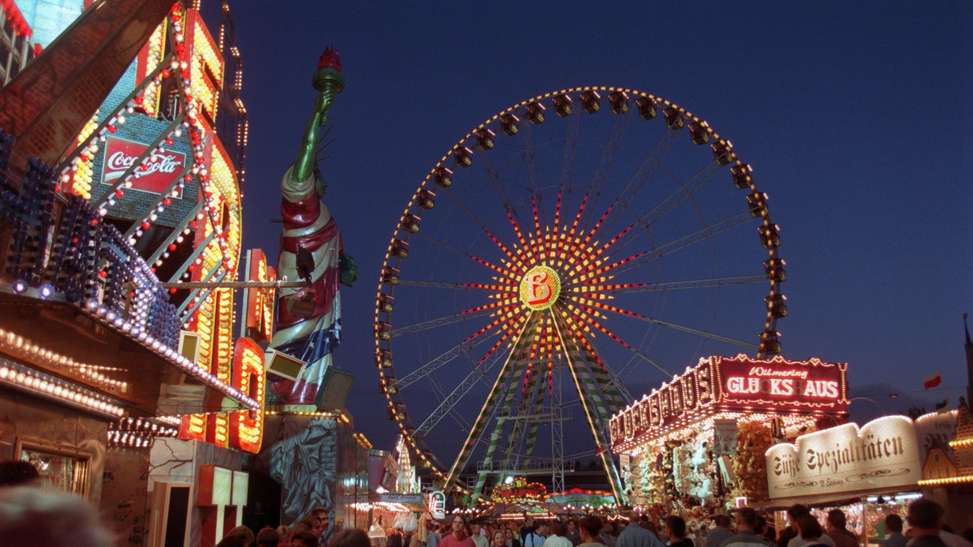 Eine bunt beleuchtete Kirmes mit einem Riesenrad in den Abendstunden.