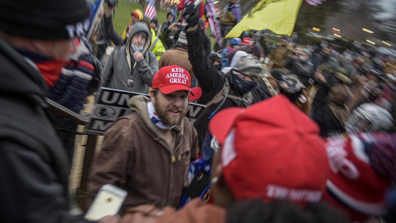 Am 6. Januar erstürmen extremistische Trump-Anhänger das Kapitol in Washington. Das Foto zeigt eine demonstrierende Menschenmenge, im Zentrum ein Mann mit Trumpanhänger-Cap.