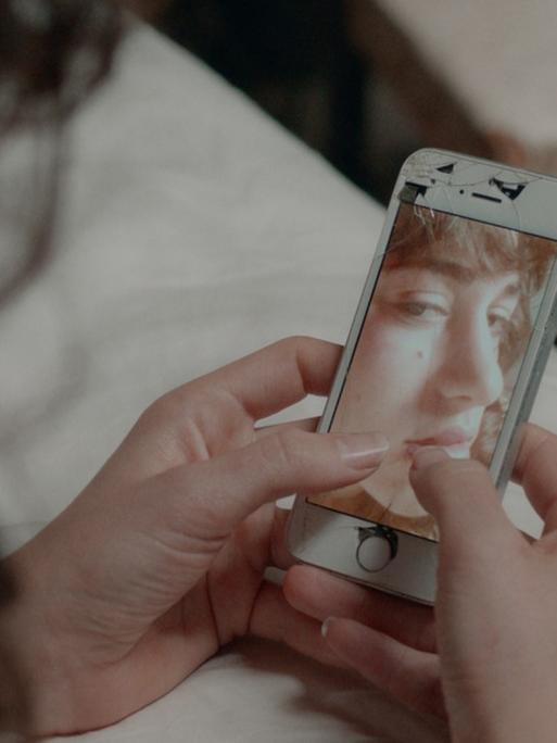 Eine Frau schaut auf ein Handy, auf dem ein Foto einer Frau zu sehen ist.