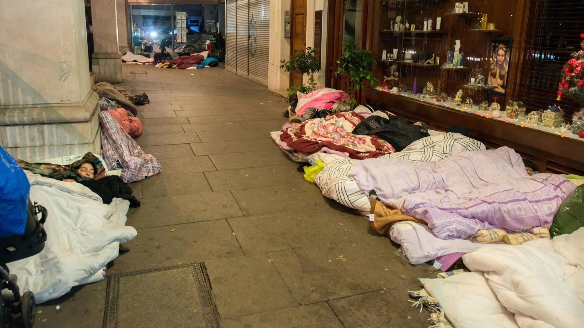 Mehrere Obdachlose liegen in London in einer kleinen Straße mit Geschäften.