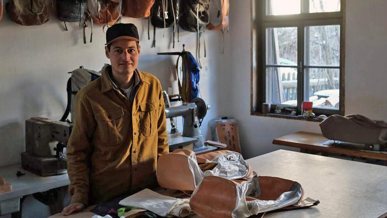Leander Angerer steht in seiner Werkstatt vor von ihm designten Rucksäcken.