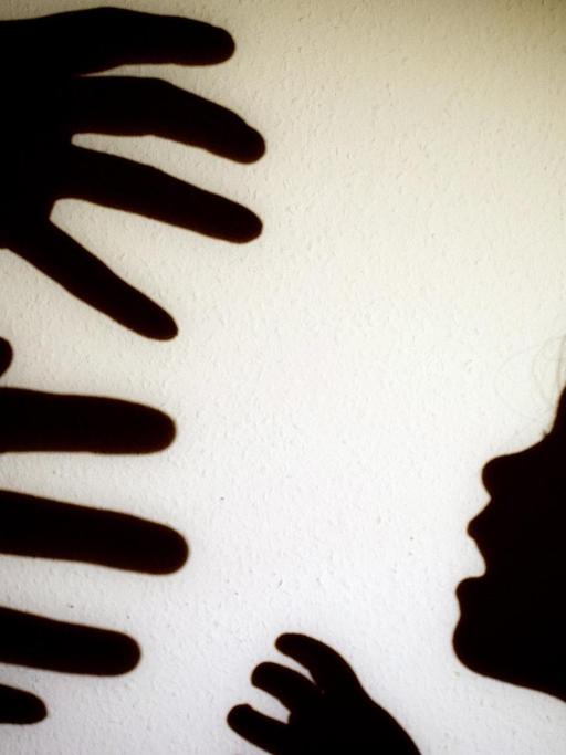 Das Bild zeigt Schattenrisse von drohenden Händen eines Erwachsenen und den Schatten eines Kinderkopfes.