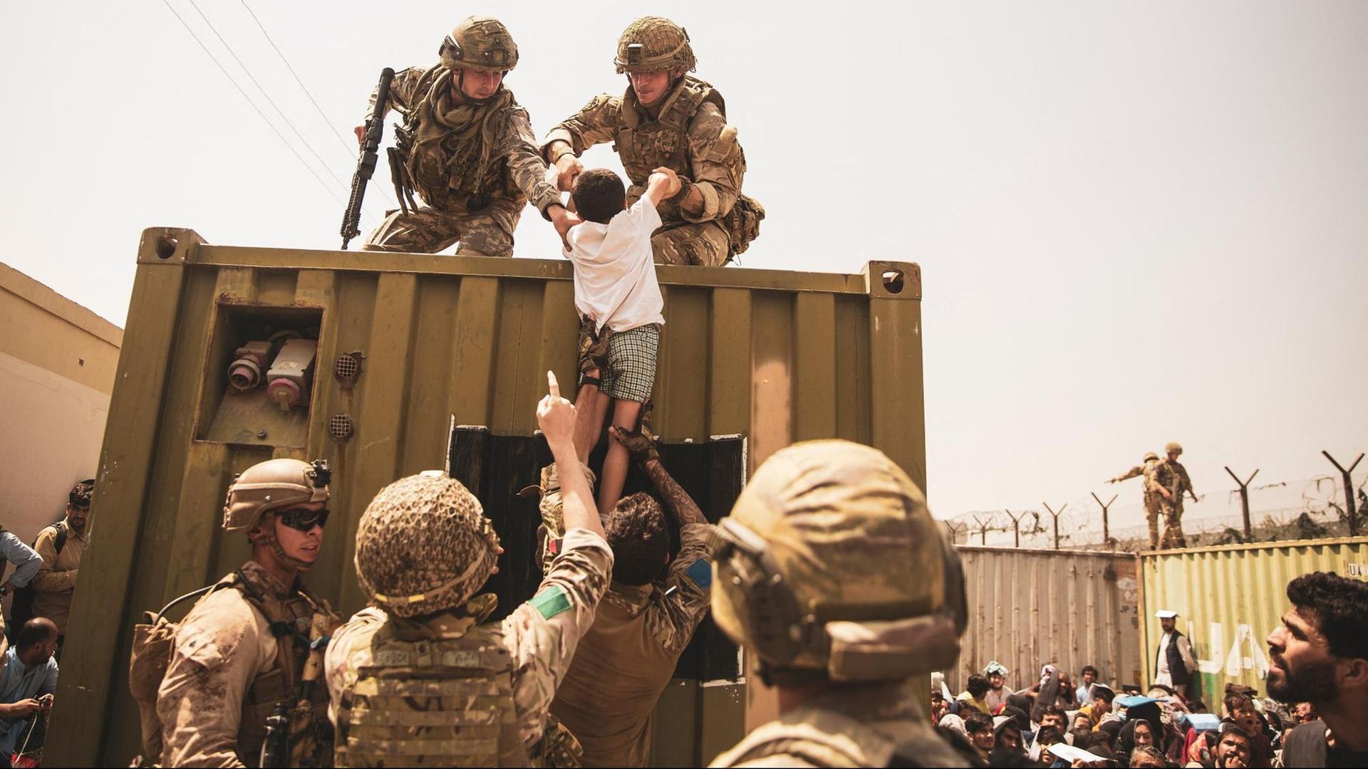 Britische Koalitionstruppen, türkische Koalitionstruppen und US-Marines helfen einem Kind während einer Evakuierung am internationalen Flughafen Hamid Karzai in Kabul.