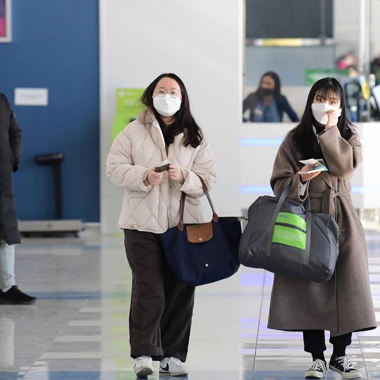 Menschen mit Schutzmasken laufen in einem Flughafen.