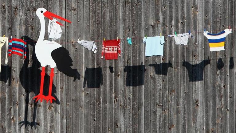 Babykleidung und ein Storch aus Holz hängen an einer Leine vor einem Bauernhof in Apfeltrang (Bayern). Der Schmuck soll, nach altem Brauch, den frisch verheirateten Bewohnern des Hauses zu reichem Kindersegen verhelfen.