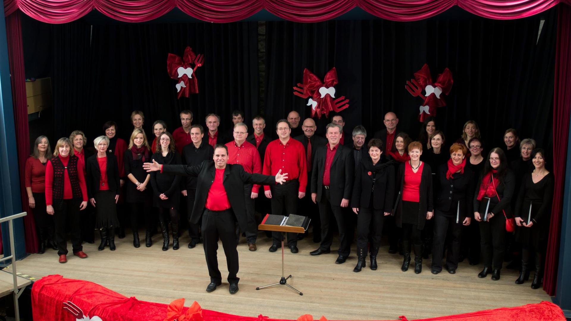 Der Chor in roter und schwarzer Kleidung auf einer Bühne.