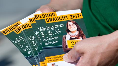 Zu sehen sind die Flyer des Volksbegehrens in grün und gelb, darauf steht "Bildung braucht Zeit."