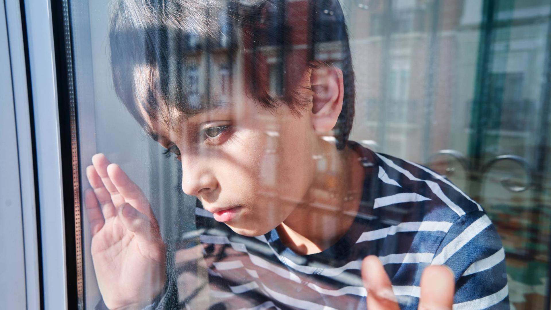 Ein Junge schaut unglücklich aus dem Fenster. (Symbolfoto)