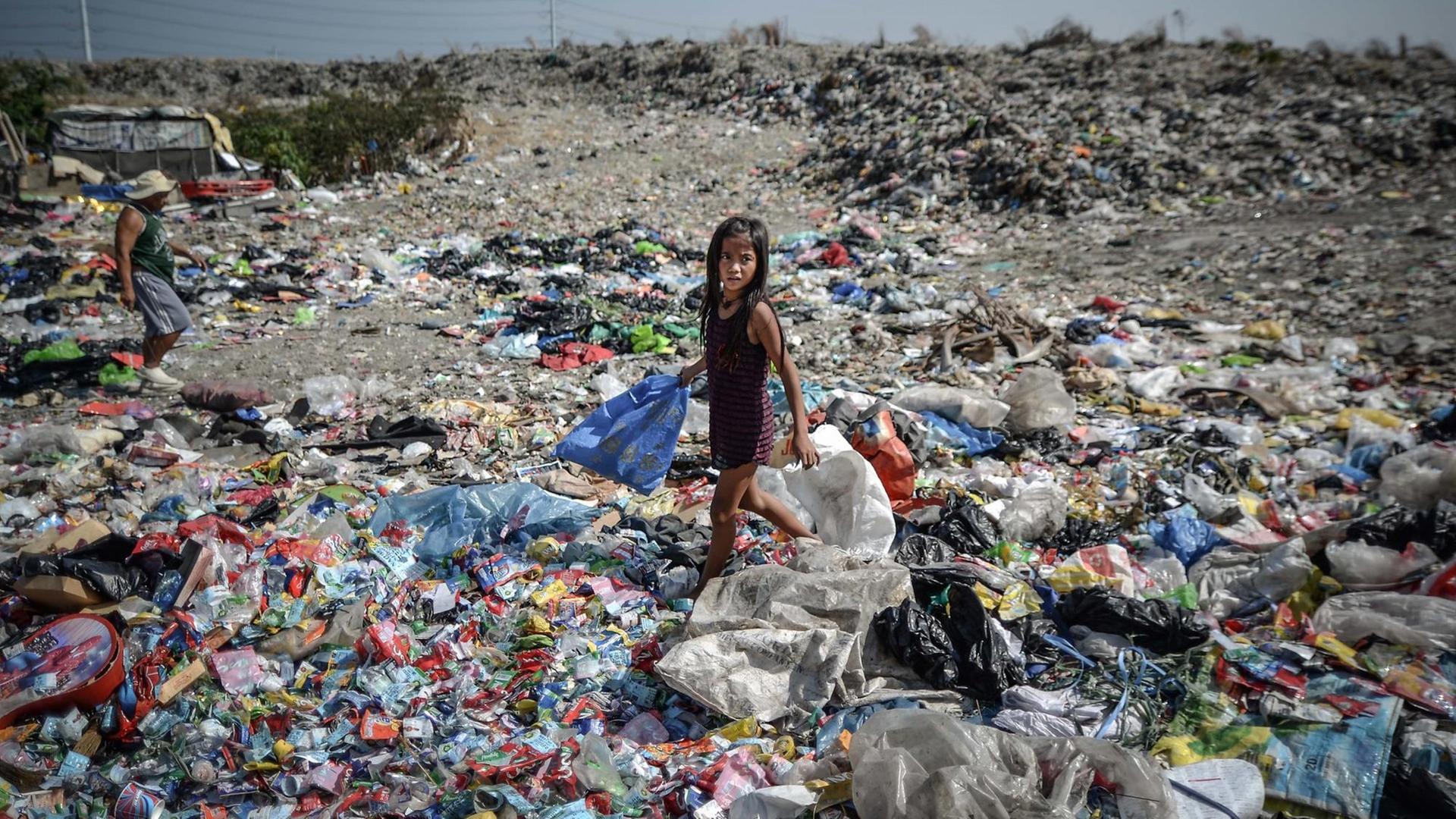 Ein Mädchen läuft mit einer Plastiktüte in der Hand über eine Müllhalde auf den Philippinen