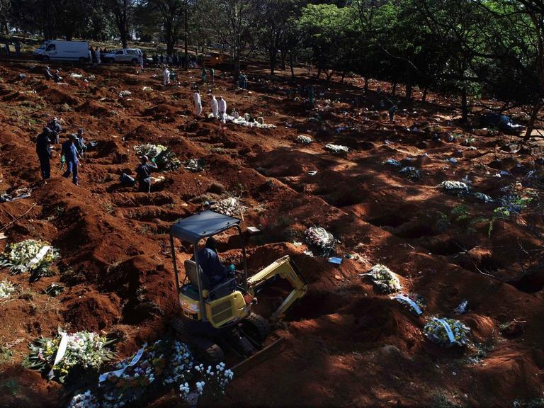 Luftaufnahme einer Drohne. Auf einem Feld sind zahlreiche Gräber für Coronaopfer ausgehoben worden. Auf einzelnen Gräbern liegen Kränze.