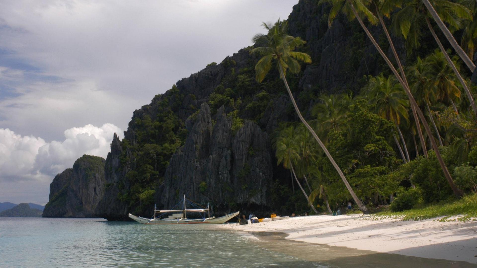Ein Boot liegt an einem weißen Sandstrand in einer Bucht, die zur philippinische Provinz Palawan gehört.