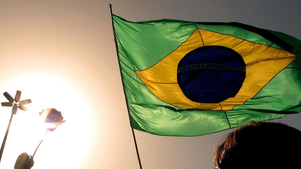 Im Sonnenuntergang hält ein Mann die Flagge von Brasilien.