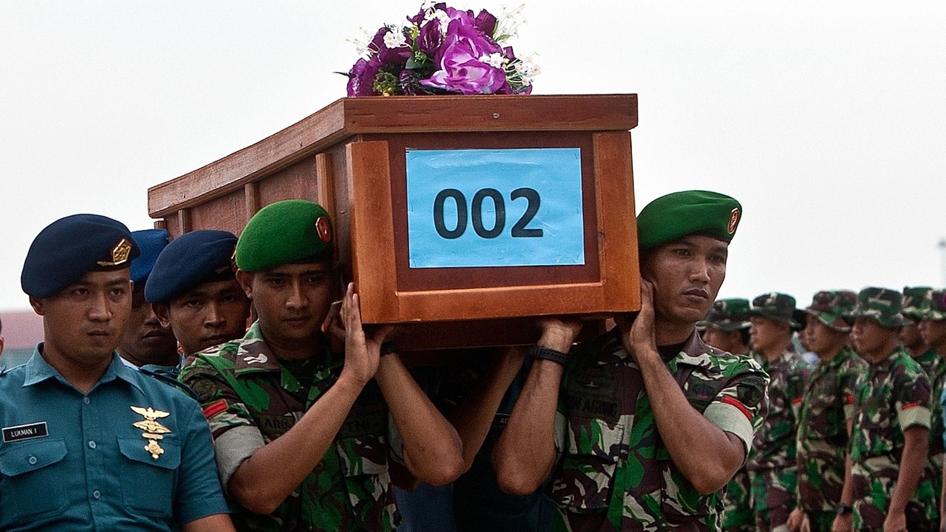 Indonesische Soldaten tragen einen Holzsarg mit einem der ersten gefundenen Opfer des Air-Asia-Flugzeugabsturzes auf dem Flughafen in Surabaya