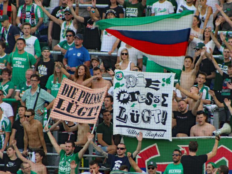 Blick auf die Fantribüne von Rapid Wien, Fans halten Plakate hoch mit der Aufschrift "Die Presse lügt".