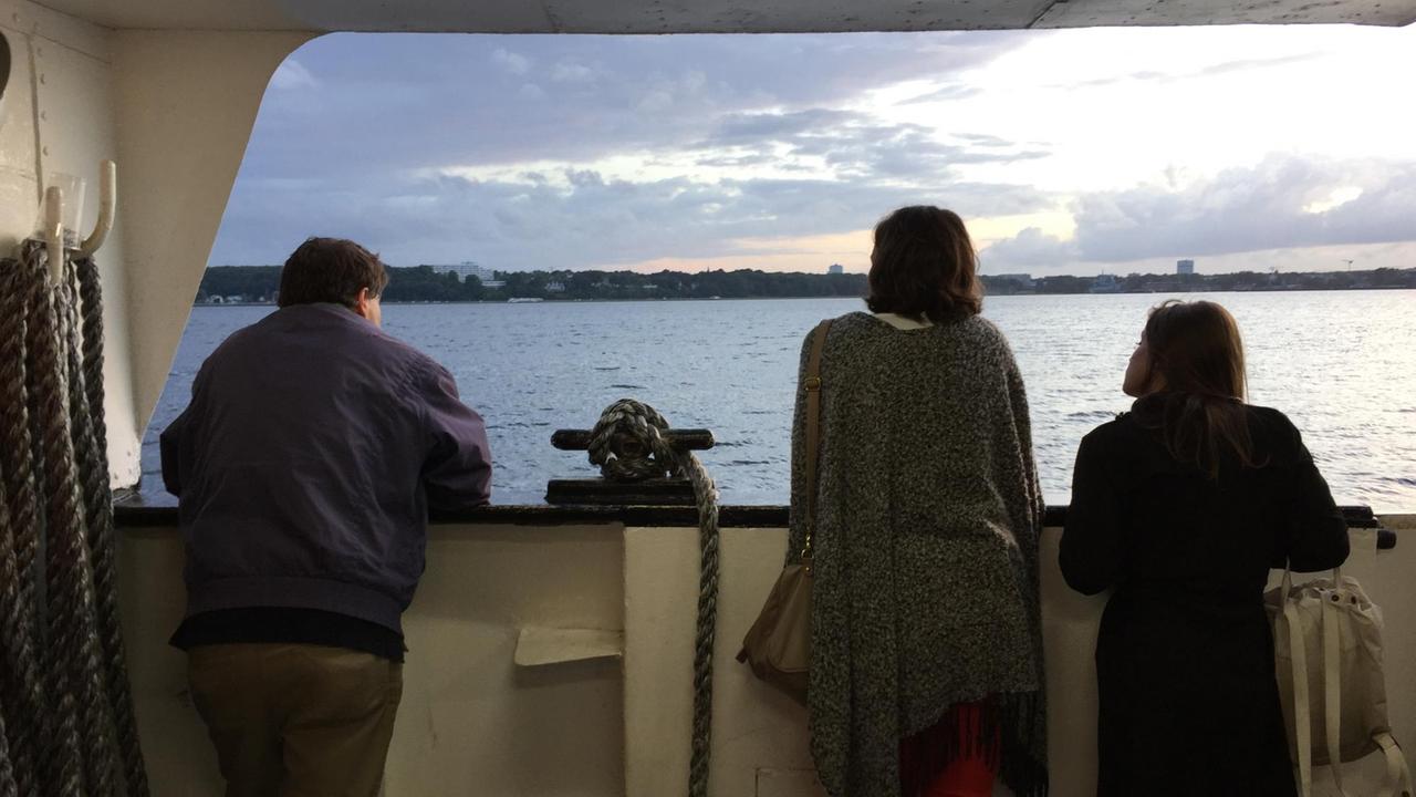 Zwei Frauen und ein Mann stehen an der Reeling des Schiffes und schauen aufs Meer.
