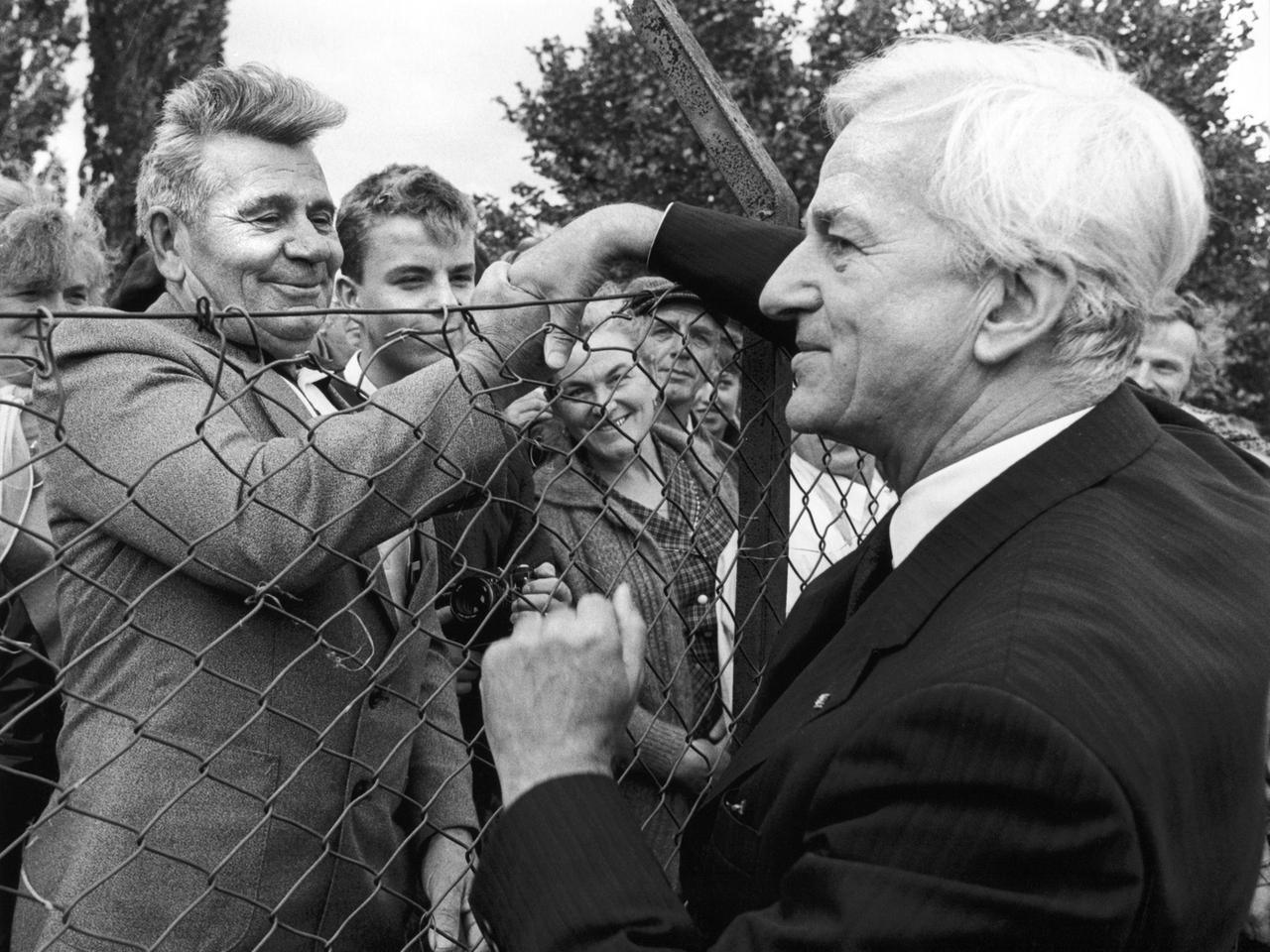 Begrüßung über den Zaun hinweg: Stundenlang haben die Aussiedler am 06.10.1987 auf die Ankunft von Richard von Weizsäcker (r) gewartet. Der Bundespräsident besucht die Institution anlässlich des 30-jährigen Bestehens der Friedland-Hilfe.