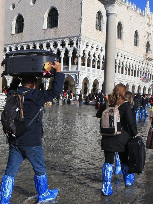 Venedig leidett im November 2019 unter einem der schlimmsten Überschwemmung nach Starkregen. Das Foto zeigt Leutein Gummistiefeln und Schutzmanschetten, die ihre Taschen teils über dem Kopf tragen.