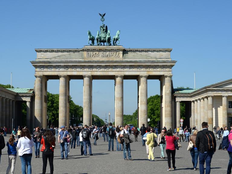Ansicht des Brandenburger Tors vom Pariser Platz aus, davor zerstreut Menschen, dahinter in der Flucht die Siegessäule