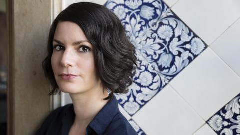 Porträtaufnahme von Isabelle Lehn vor eine Wand mit blau-weißen Fliesen