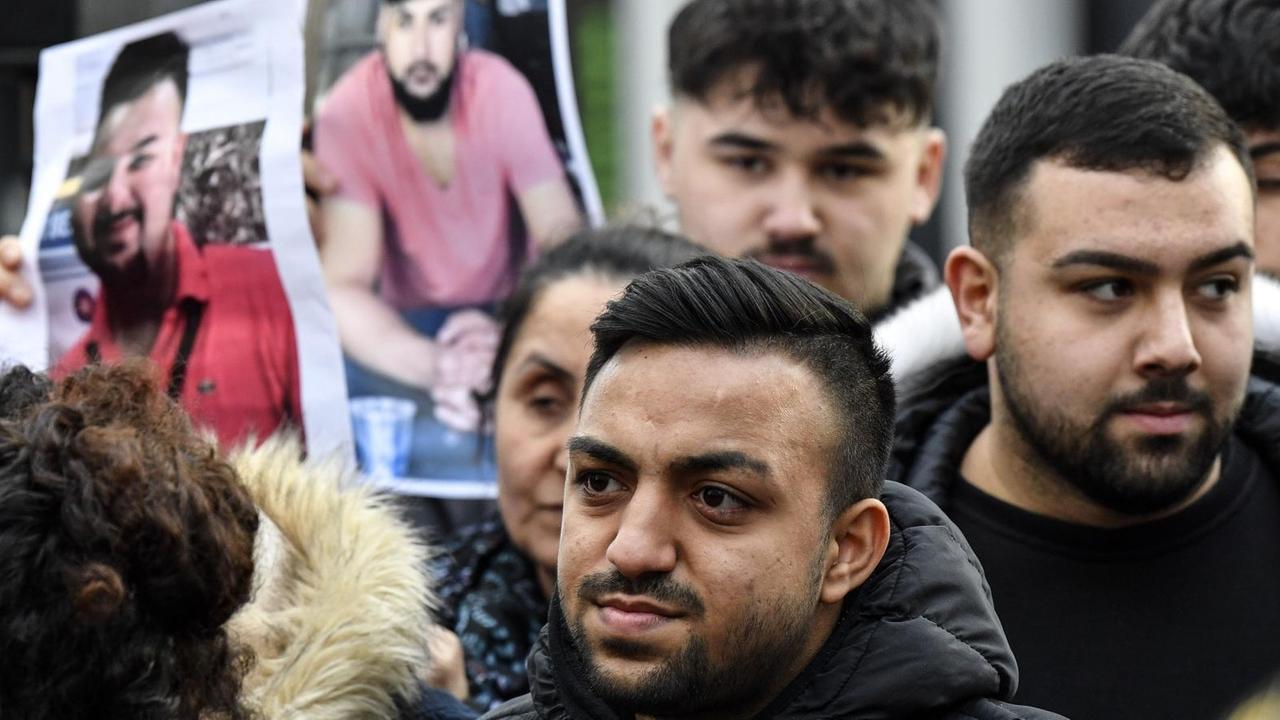 Freunde und Verwandte der Opfer des rechten Terroranschlags von Hanau stehen in einer Gruppe und halten Bilder hoch