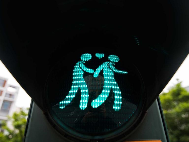 Eine Ampel zeigt ein homosexuelles Paar, das Händchen hält.
