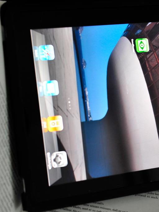 Ein iPad mit Apps auf dem Bildschirm liegt auf einem aufgeschlagenen Buch.