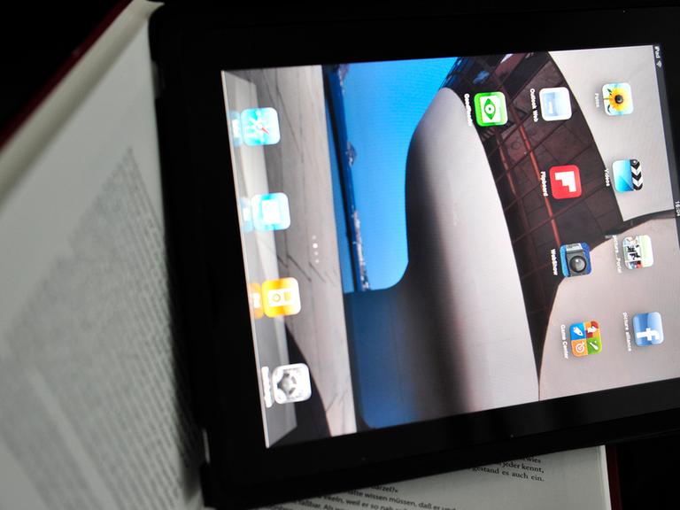 Ein iPad mit Apps auf dem Bildschirm liegt auf einem aufgeschlagenen Buch.