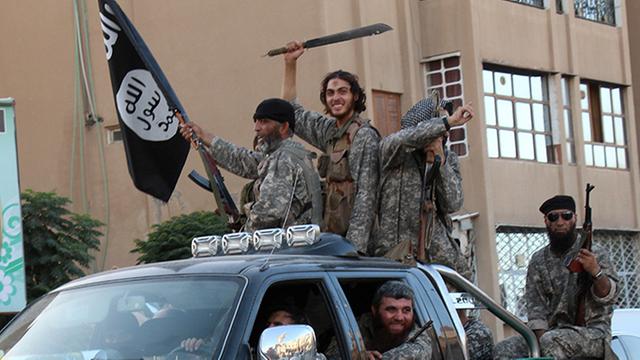 Angebliche Kämpfer der Terrorgruppe IS in der syrischen Stadt ar-Raqqa sitzen bewaffnet in und auf einem Auto.