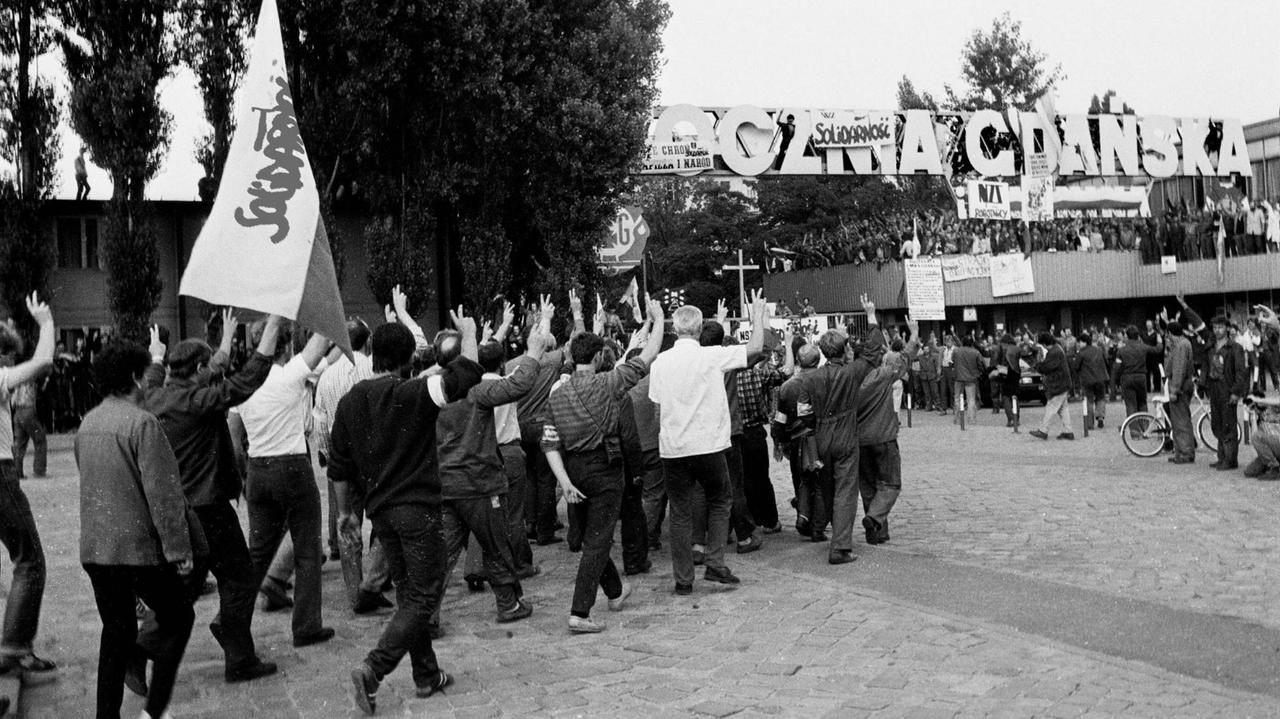 Streikende Arbeiter laufen mit geschwenkten Solidarność-Fahnen durch das Werktor der Lenin Werft in Danzig.