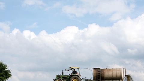 Ein Trecker mit Güllewagen fährt über ein Feld und verteilt Gülle.