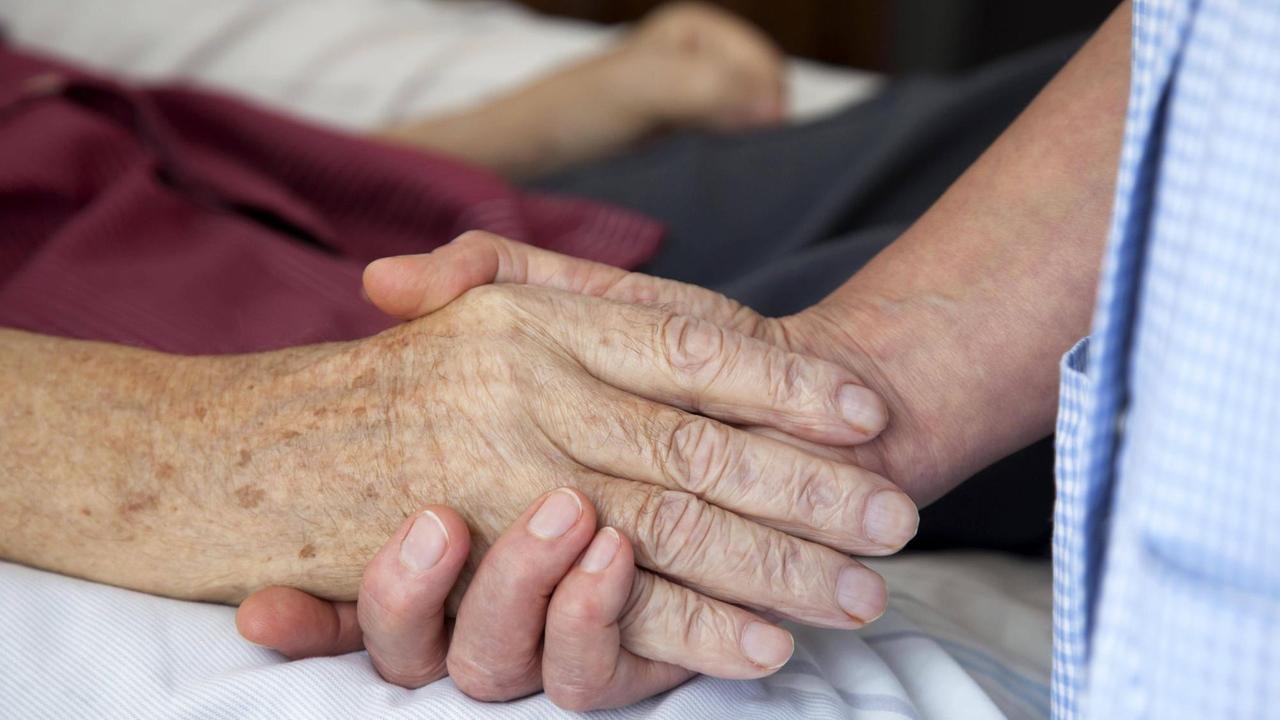 Die Hand einer Pflegerin haelt die Hand eines alten Mannes. 