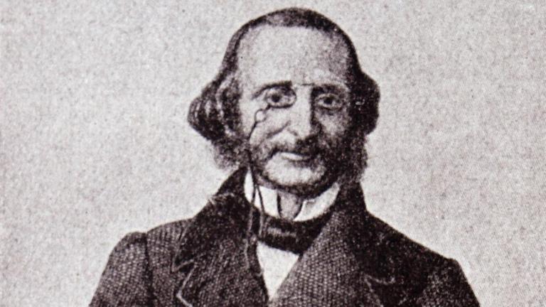 Ein Porträt von Jacques Offenbach. Er trägt einen langen Mantel, auf der Nase seinen Zwicker.