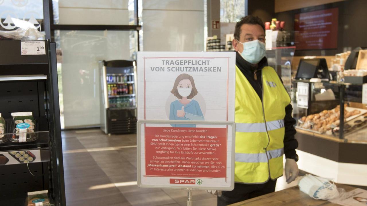 In einem Supermarkt in Österreich steht ein Mitarbeiter hinter einer Theke und verteilt Schutzmasken.