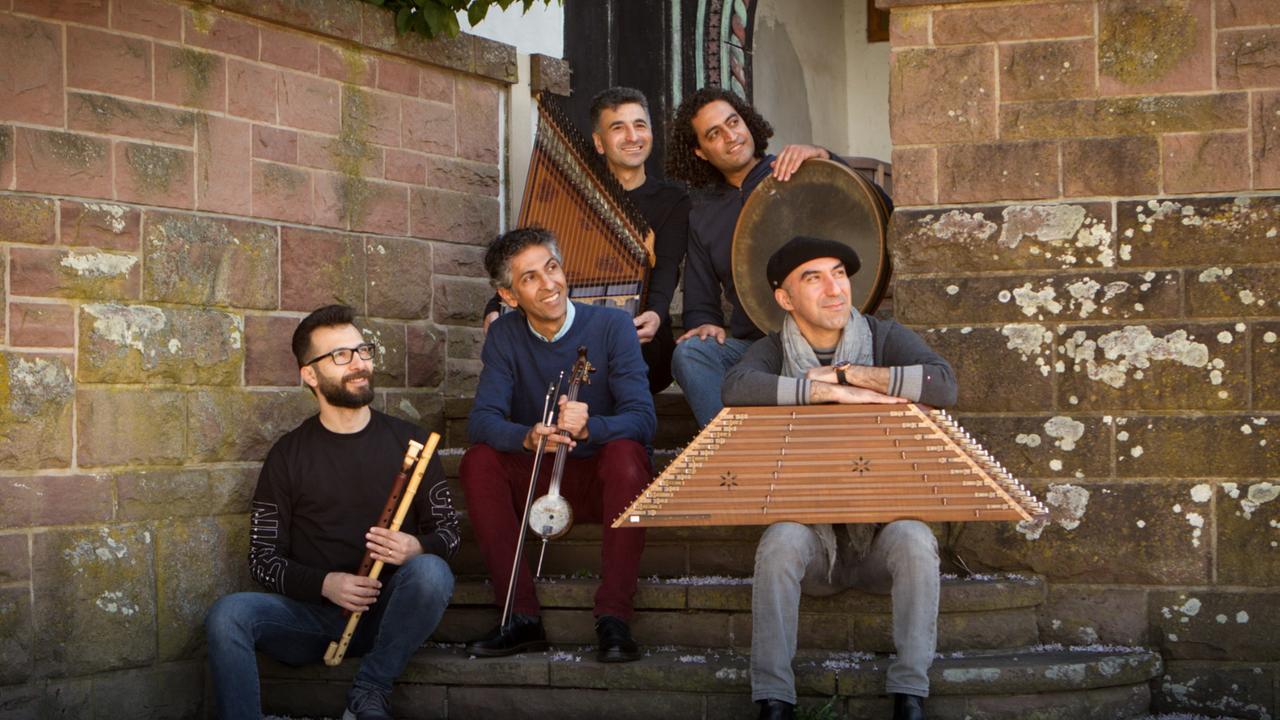 Die fünf Musiker sitzen mit ihren Instrumenten auf einer Treppe zu einem alten Gebäude